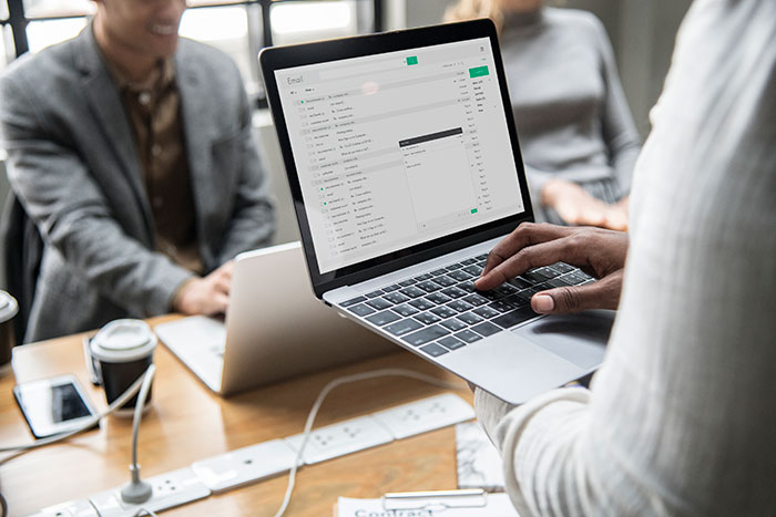 A person holding a laptop in an office, emails open, while colleagues discuss ticket escalation.
