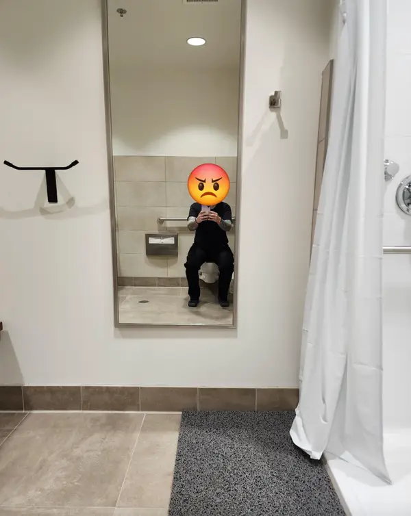 Person with angry emoji on face taking a mirror selfie in a restroom