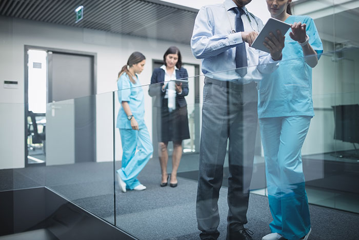 Office workers and nurses discussing in a modern hallway, highlighting workplace dynamics and compliance issues.