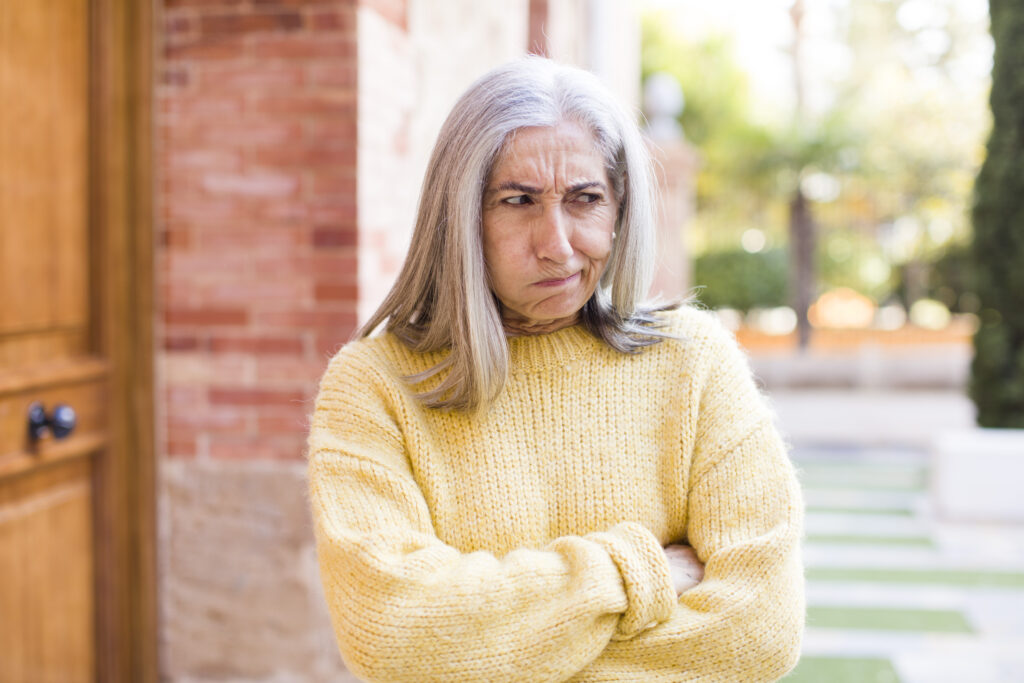Grumpy woman in a yellow sweater standing outside, embodying petty revenge theme.