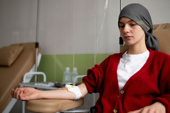 Person receiving medical treatment, wearing a red cardigan and headscarf, illustrating a serious health diagnosis.