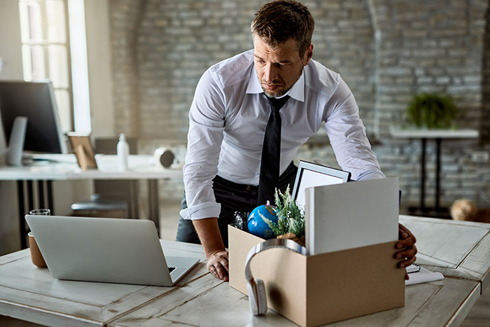 A worker packing belongings in a box, reflecting HR challenges faced with a supervisor observing.