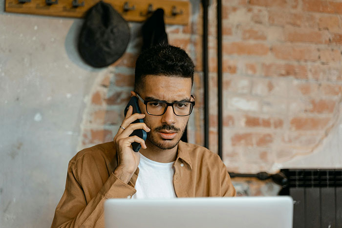 Man in glasses using a laptop, talking on the phone, representing worker interactions with HR and supervisors.