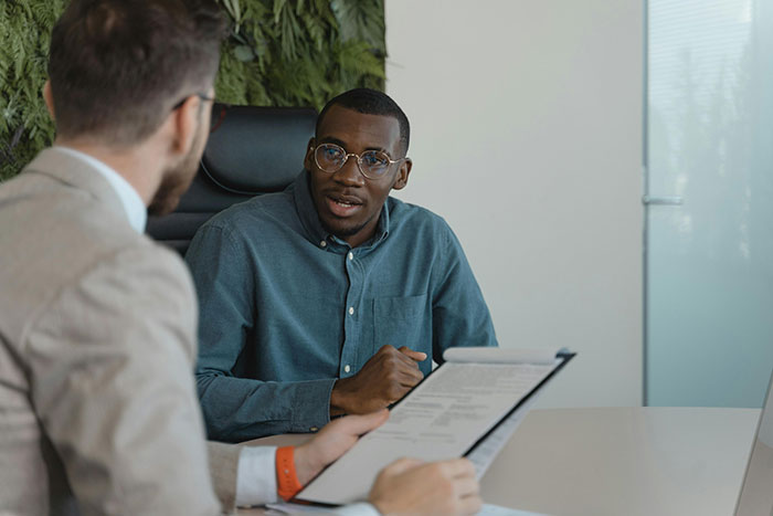 Man in a blue shirt discusses with another man holding a document, illustrating HR challenges in an office setting.