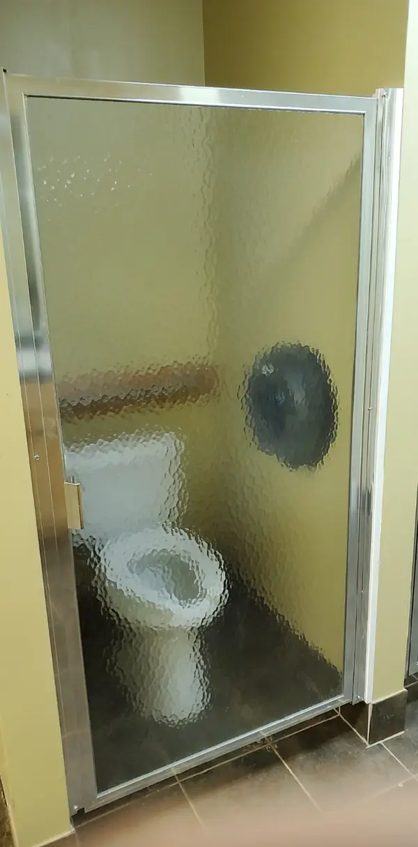 Bathroom stall with a clear, wavy glass door, showing a visible toilet inside