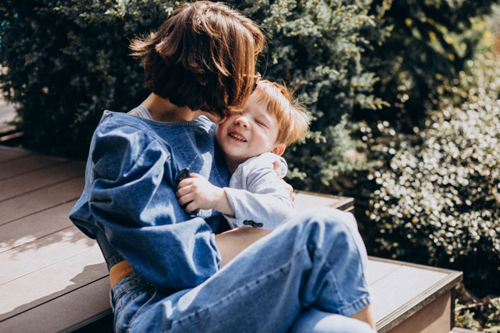 Woman sitting outside with her son who has autism, sharing a tender moment while embracing and smiling together.