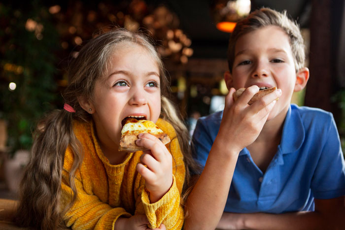 Young children eating pizza, illustrating challenges related to food talk and autism triggers in family dynamics.