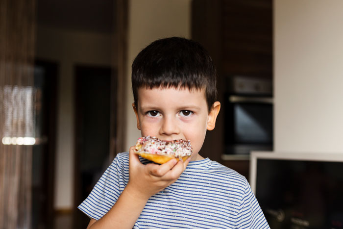 Young boy eating a doughnut in a home kitchen, illustrating food talk triggers related to son’s autism challenges.