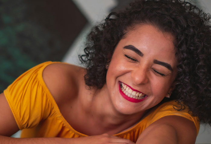 Woman in a yellow top laughing joyfully, highlighting karma's impact in a social situation.