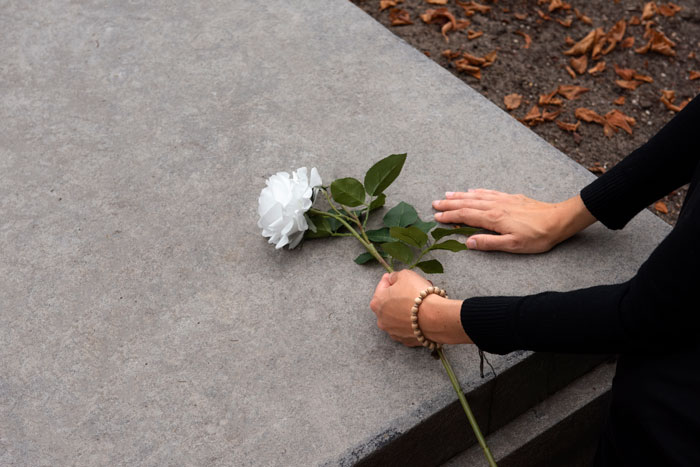 Person placing a white rose on a gravestone, symbolizing loss and remembrance of a coworker.
