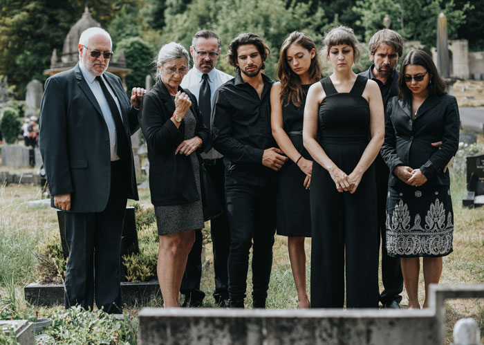 Group of people in formal attire mourning at a cemetery.