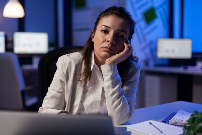 Woman in an office looking at a laptop, appearing thoughtful.