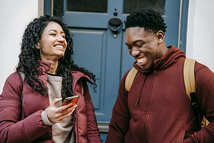 Two friends smiling and sharing a light moment outside a building, expressing friend regret and best friend confession.