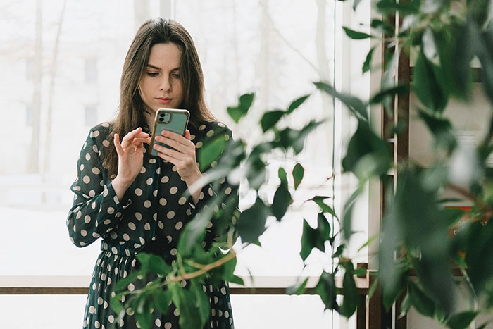 Child-free woman on vacation, using her phone, surrounded by plants, enjoying a peaceful moment indoors.