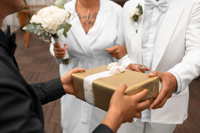 Wedding gift exchange with couple in white attire, bride holding flowers, highlighting gift-related tension.