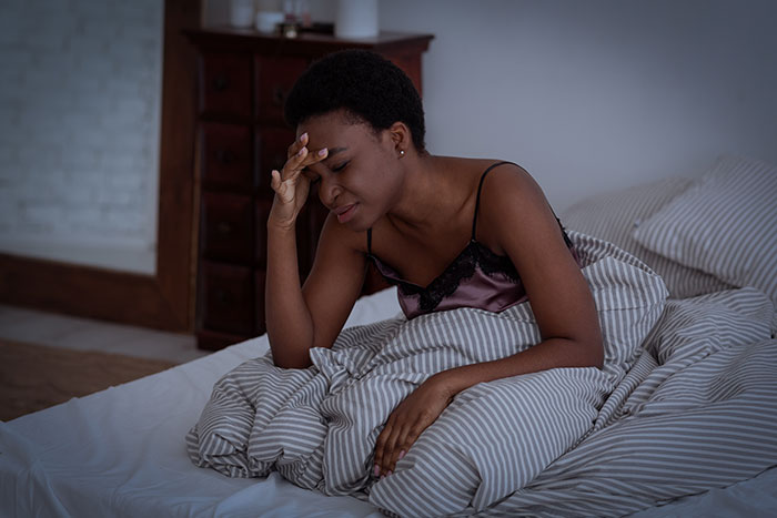 Woman in bedroom looking frustrated, covering her face, representing a clever woman dealing with loud downstairs neighbor.